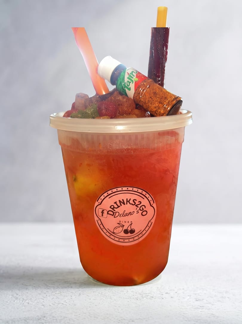 A red drink in a clear plastic cup with a Tajin bottle, candy, and a straw.