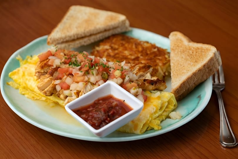 Breakfast plate with scrambled eggs, hash browns, chicken with pico de gallo, salsa, and toast.