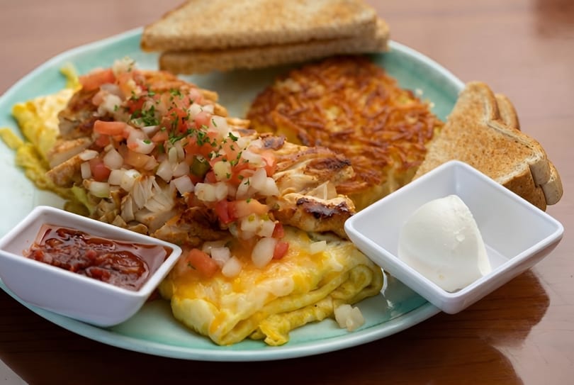 A breakfast plate with an omelet topped with salsa, hash browns, toast, and sides of jam and butter.