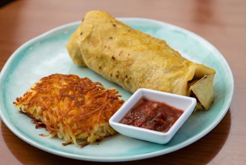 Breakfast burrito with hash browns and a side of salsa on a light blue plate.