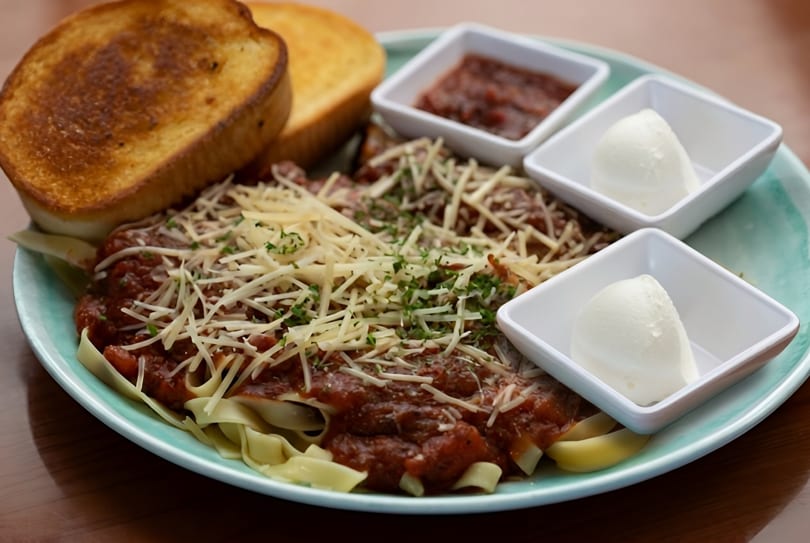 Pasta with meat sauce, shredded cheese, and parsley, served with toast, salsa, and sour cream.